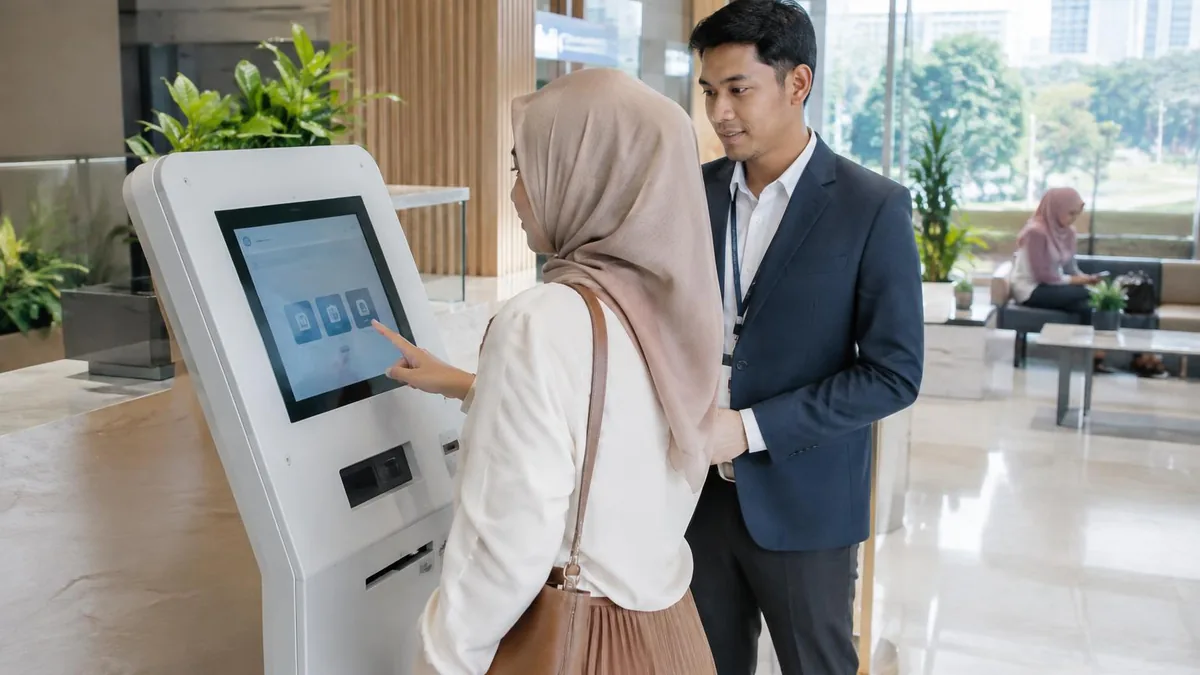 Kiosk mandiri modern di area layanan bank dengan nasabah yang sedang menggunakannya.