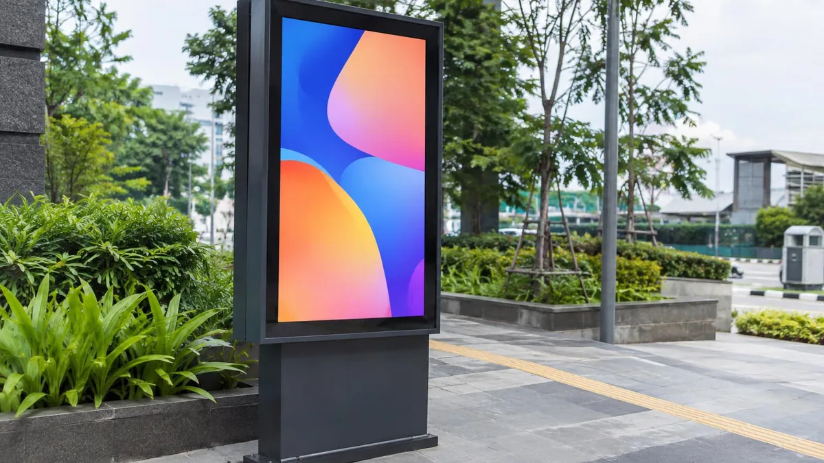 Perangkat digital signage outdoor generik di area komersial terbuka dengan layar bergambar abstrak